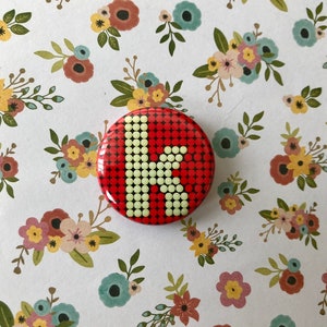 May include: A red button with a white letter K in the center. The letter K is made up of small white dots on a red background.
