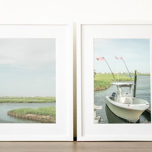 May include: Two framed photographs of a coastal scene. The left photo shows a marsh with green grasses and water. The right photo shows a white boat docked in a waterway with two American flags flying.