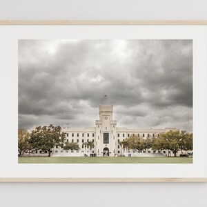 May include: A framed photograph of a large white building with a clock tower under a cloudy sky. The building has a symmetrical design with many windows and a row of trees in front.