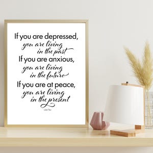 May include: A framed print with a gold frame featuring a quote by Lao Tzu in black script: "If you are depressed, you are living in the past. If you are anxious, you are living in the future. If you are at peace, you are living in the present."
