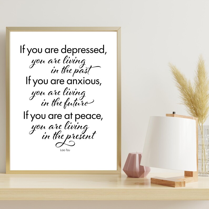 May include: A framed print with a gold frame featuring a quote by Lao Tzu in black script: "If you are depressed, you are living in the past. If you are anxious, you are living in the future. If you are at peace, you are living in the present."