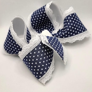 May include: Navy blue polka dot hair bows with white lace trim. The bows are made of fabric and feature a classic polka dot pattern. The bows are a cute accessory for any hairstyle.