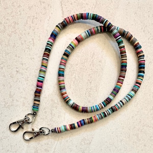 May include: A colorful beaded lanyard with two silver lobster clasps. The lanyard is made of small, round, multi-colored beads.