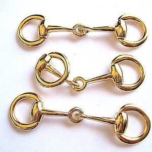 May include: Three gold-toned metal horse bit-shaped clasps. Each clasp has a round ring on each end and a straight bar connecting the rings.