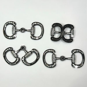 May include: Four black metal buckles with clear rhinestone accents. The buckles are in different shapes and sizes.