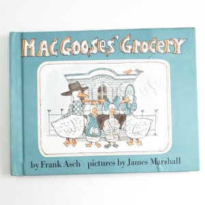 May include: A blue book with the title "Mac Goose's Grocery" in orange lettering. The cover features an illustration of four geese in front of a store with a sign that reads "Mac Goose's". The book is by Frank Asch with pictures by James Marshall.