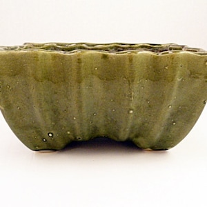 May include: A green ceramic planter with a wavy, scalloped rim and a slightly curved base. The planter has a speckled glaze and a matte finish.