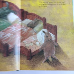 May include: A children's book illustration shows a brown rabbit standing near a red bed with floral bedding. The text on the page reads, "Oh what's beautiful morning!" and "says Mrs. Josephine as she slips out of bed."