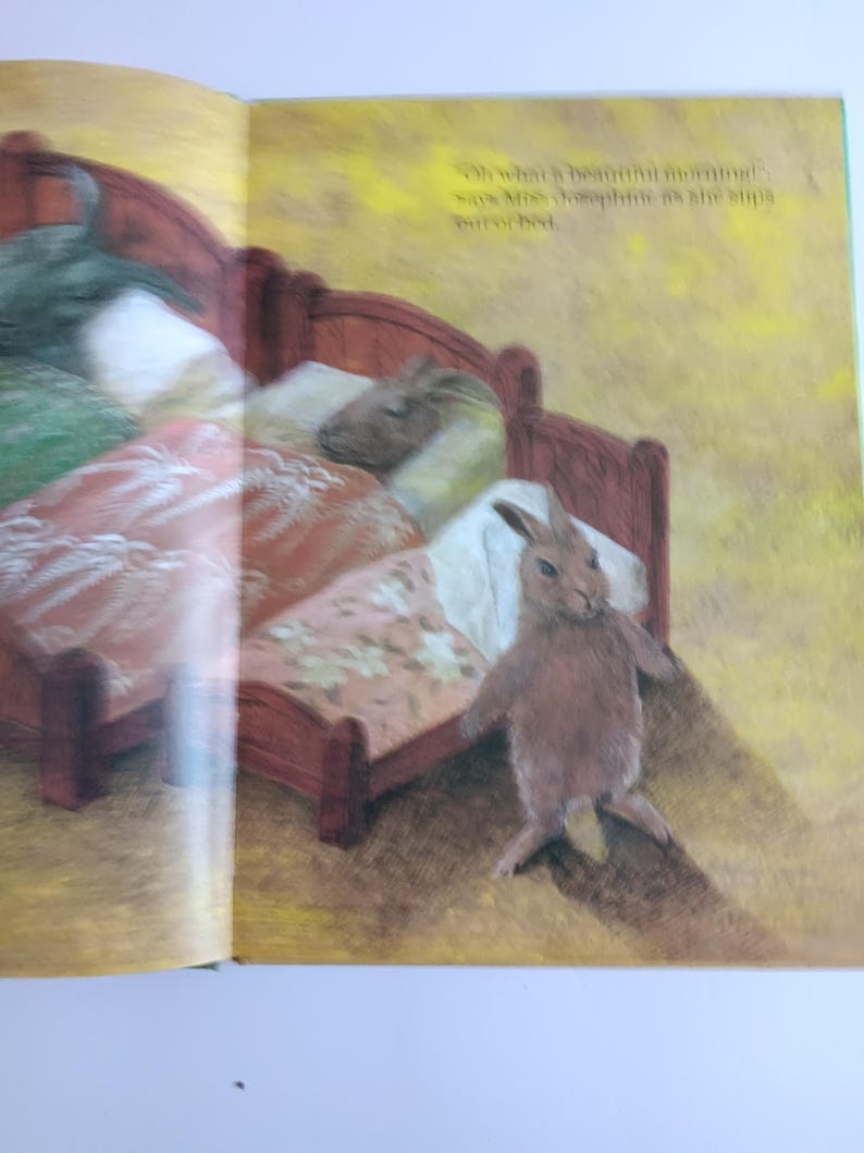 May include: A children's book illustration shows a brown rabbit standing near a red bed with floral bedding. The text on the page reads, "Oh what's beautiful morning!" and "says Mrs. Josephine as she slips out of bed."