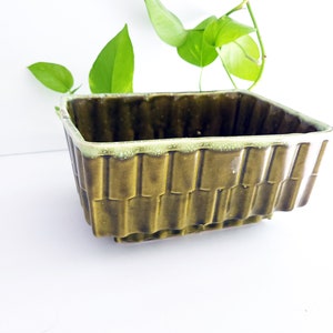 May include: A square green ceramic planter with a textured, ribbed design. The planter has a light green glaze around the top edge.