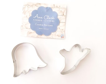 Könnte beinhalten: Zwei silberfarbene Geister-Ausstecher. Ein Geist hat einen wellenförmigen unteren Rand, der andere eine vereinfachte Form. Im Hintergrund befindet sich eine Karte mit dem Text "Ann Clark Cookie Cutters Cookie Recipes Made in Vermont".