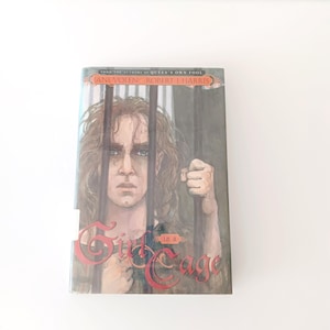 May include: A hardcover book titled "Girl in a Cage" by Jane Yolen and Robert J. Harris. The cover art features a young person with long hair behind bars, with the title in red script.