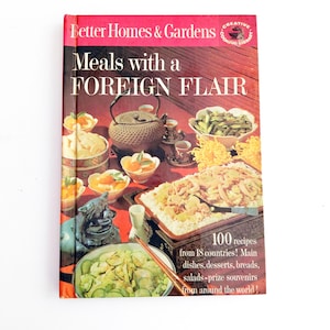 Könnte beinhalten: Ein Better Homes & Gardens Kochbuch mit dem Titel Meals with a FOREIGN FLAIR. Das rote Cover zeigt ein Foto verschiedener Gerichte, einer Teekanne und Essstäbchen. Der Text lautet 100 recipes from 18 countries! Main dishes, desserts, breads, salads-prize souvenirs from around the world!
