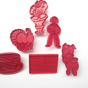Può includere: Set di sei tagliapasta in plastica rossa, con un tacchino, Babbo Natale, un maiale, una persona, una torta e una bandiera americana.