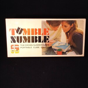 May include: A box for the Tumble Numble game, a portable cube edition of the cross-number game. The box shows a couple playing the game with a timer and a cube.