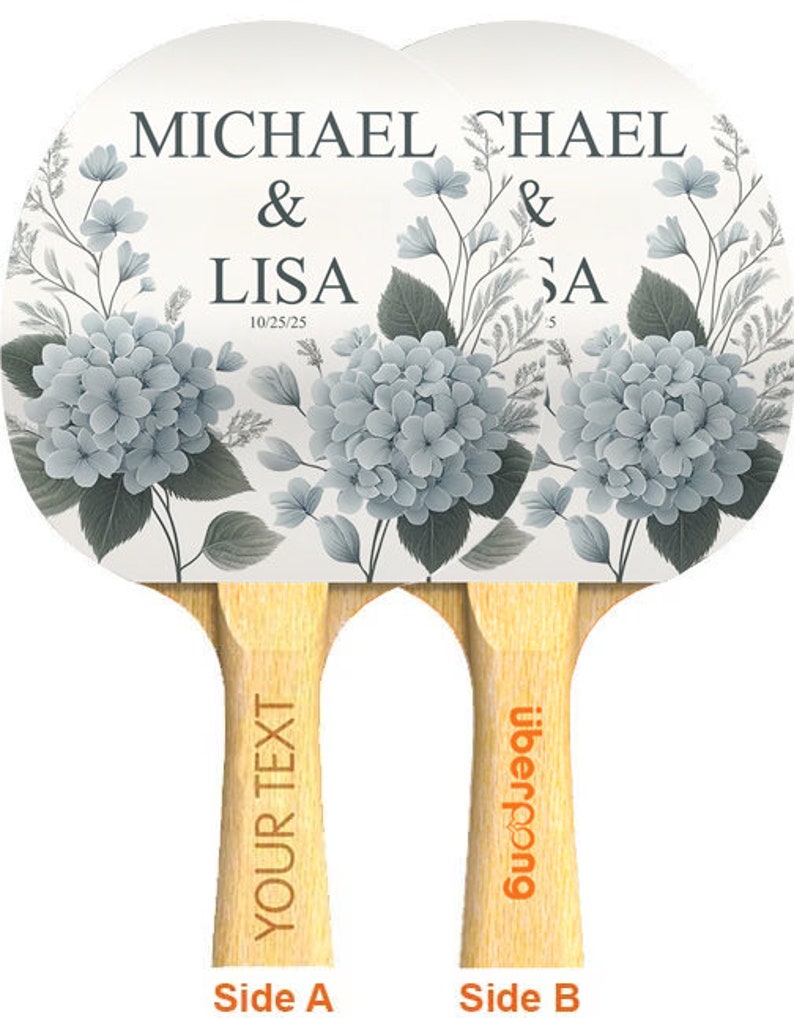 Może przedstawiać: Para białych rakiet do tenisa stołowego z kwiatowym wzorem z niebieskimi hortensjami. Rakietki są spersonalizowane nazwiskami "Michael & Lisa" i "Chael & Sa" oraz datami "10/25/25" i "5". Uchwyty są oznaczone "Your Text" i "Uberpong".