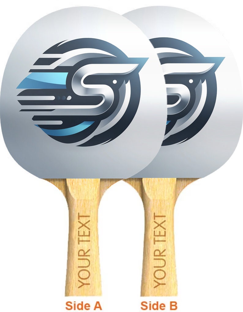Może przedstawiać: Dwie białe paletki do tenisa stołowego z czarno-niebieskim logo na powierzchni paletki. Logo to stylizowana litera "S" z skrzydłem. Paletki mają drewniane uchwyty z nadrukowanym tekstem "YOUR TEXT". Tekst "Side A" i "Side B" jest nadrukowany pod paletkami.