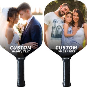 May include: Two custom designed pickleball paddles with images of a wedding couple and a family. The paddles are black with white text that says "CUSTOM IMAGE / TEXT".