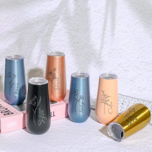 Könnte beinhalten: Sechs personalisierte Edelstahlbecher mit Blumendesigns und Namen. Die Becher sind in verschiedenen Farben erhältlich, darunter Gold, Roségold, Schwarz, Blau und Pfirsich.