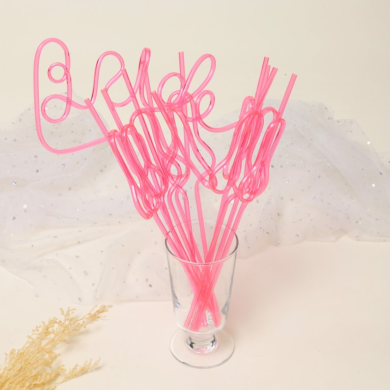 May include: Pink plastic straws shaped to spell out the word "bride" in a glass vase. The straws are a fun and festive addition to a bridal shower or wedding.