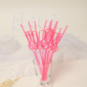 May include: A set of pink bendy straws in a glass vase with a white metal sign that says "Bride".