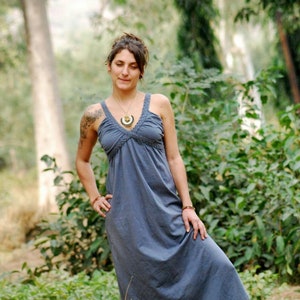 Pu&ograve; includere: Una donna indossa un lungo abito maxi grigio fluido con una semplice collana con ciondolo d'argento. &Egrave; in piedi in un'area erbosa con alberi sullo sfondo.