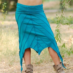 Puede incluir: Una falda azul turquesa con un diseño asimétrico único. La falda está hecha de una tela suave y fluida y tiene un ajuste holgado. La falda se muestra siendo usada por una persona con botas marrones.