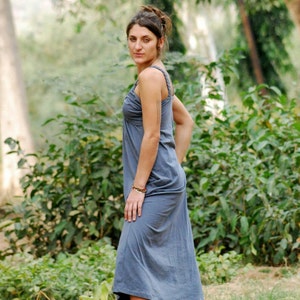 Pu&ograve; includere: Una donna con un lungo vestito grigio senza maniche in piedi in un'area erbosa con alberi sullo sfondo.