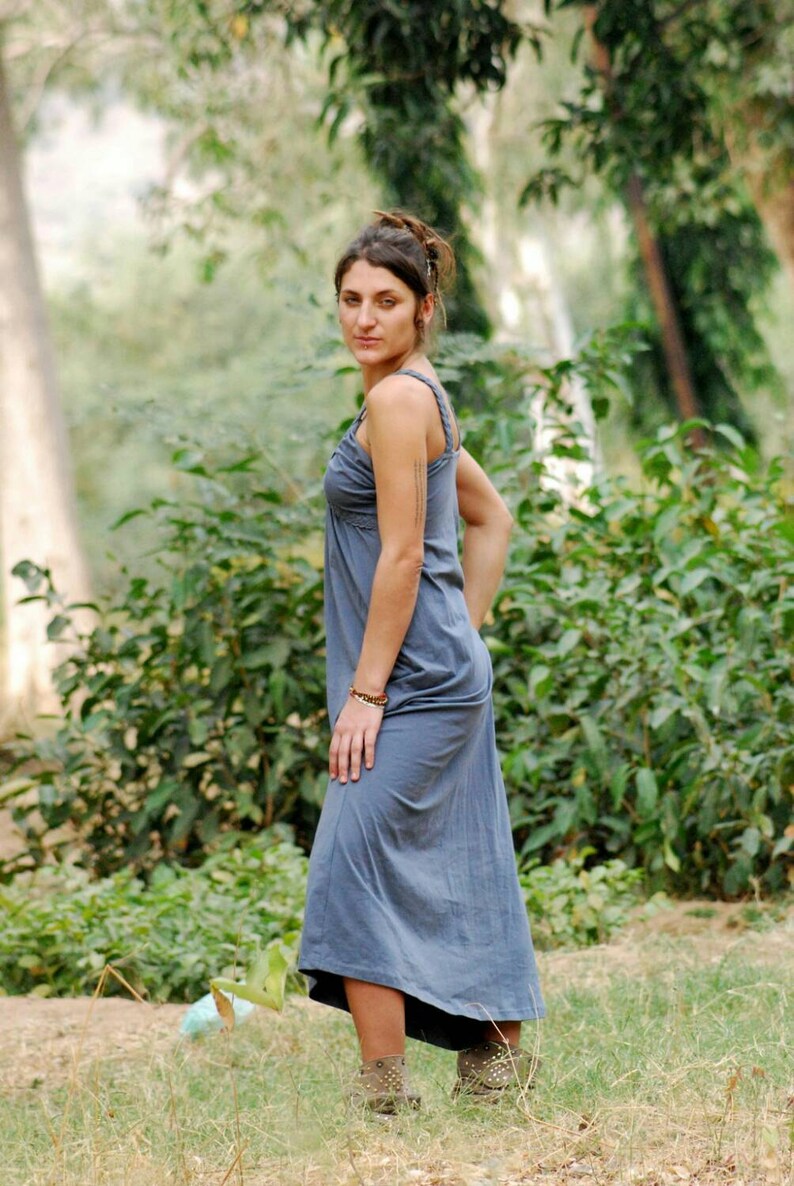 Pu&ograve; includere: Una donna con un lungo vestito grigio senza maniche in piedi in un'area erbosa con alberi sullo sfondo.