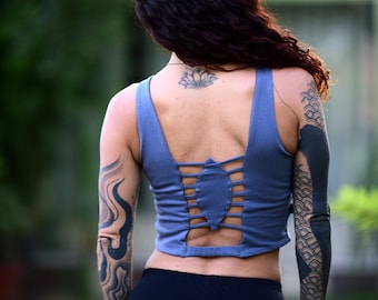 May include: A blue crop top with a unique open back design. The top has a criss-cross pattern and is paired with black leggings. The image shows a person from the back, with tattoos on the arms and a lotus flower tattoo on the back.
