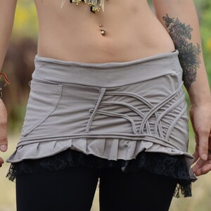 May include: A gray skirt with a ruffled hem and a black lace trim. The skirt has a unique design with a series of vertical lines and a pocket on the side.