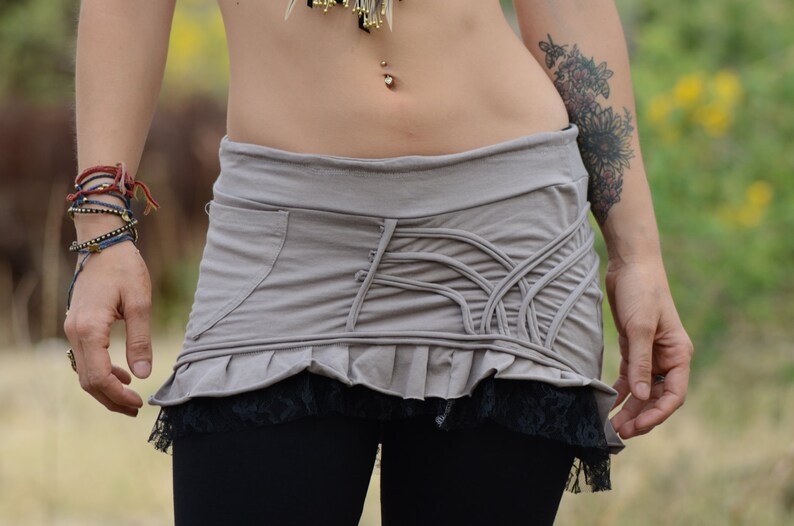 May include: A gray skirt with a ruffled hem and a black lace trim. The skirt has a unique design with a series of vertical lines and a pocket on the side.