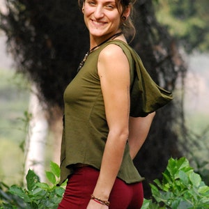 Puede incluir: Una mujer con una capucha verde y una falda roja. Est&aacute; de pie frente a un fondo verde con hojas.