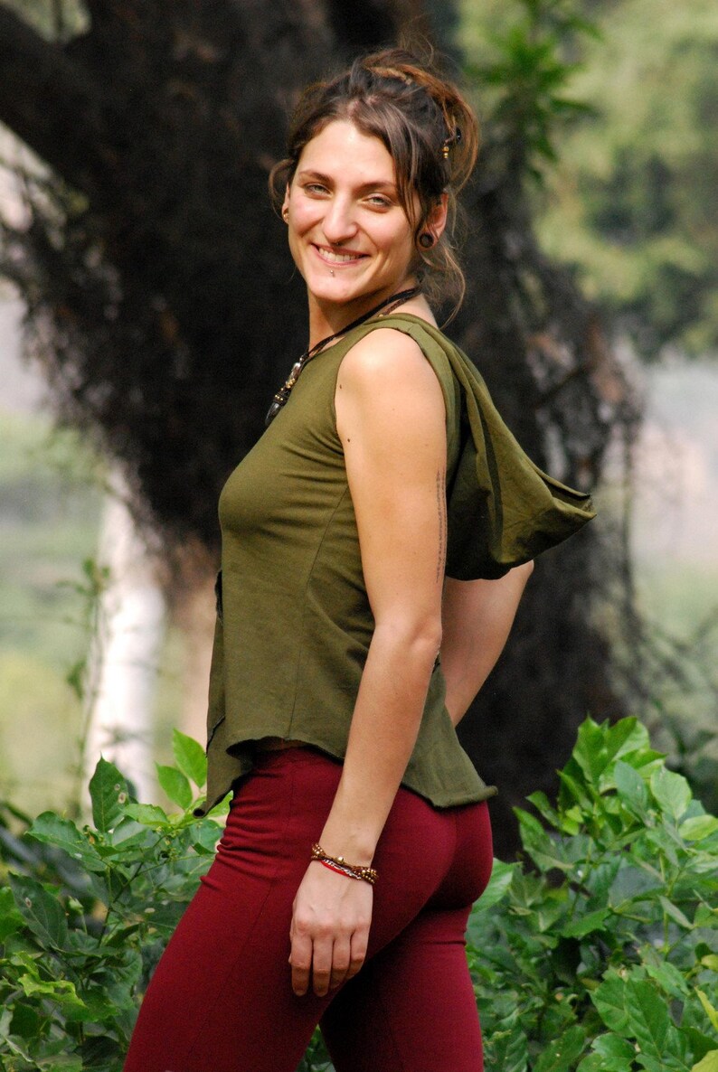 Puede incluir: Una mujer con una capucha verde y una falda roja. Est&aacute; de pie frente a un fondo verde con hojas.