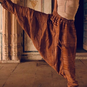 Op de afbeelding: Een paar bruine gestreepte broek met een wijde pijp en een trekkoord in de taille. De broek is gemaakt van een zachte, vloeiende stof en heeft een ontspannen pasvorm.