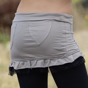 May include: A gray skirt with a ruffle hem and a heart-shaped pocket. The skirt is paired with black leggings.
