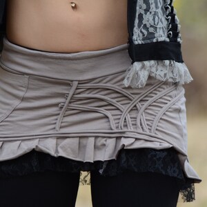 May include: A gray skirt with a lace trim and a unique design of criss-crossing fabric. The skirt has a ruffled hem and is made of a soft, comfortable material.