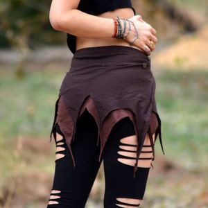 Puede incluir: Una falda marrón de envoltura con un dobladillo de flecos en capas. La falda se ata a la cintura y tiene un estilo sencillo y casual.