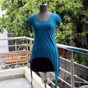 May include: A teal blue, high-low, short-sleeved shirt with a scoop neck. The shirt is on a mannequin and has a long, flowing tail.
