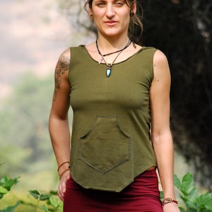 Puede incluir: Una mujer con una camisa verde sin mangas con un bolsillo y pantalones marrones. Lleva un collar con un colgante turquesa.