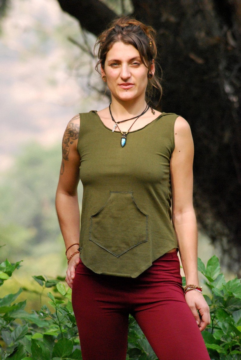 Puede incluir: Una mujer con una camisa verde sin mangas con un bolsillo y pantalones marrones. Lleva un collar con un colgante turquesa.