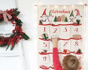 May include: A white canvas advent calendar with 13 numbered pockets, decorated with red ribbon and gnome illustrations. The calendar is labeled "Cornelius".