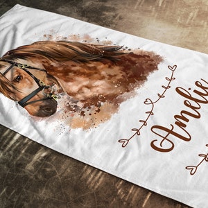May include: A white beach towel with a watercolor painting of a brown horse with a bridle. The horse's head is turned to the side and its eyes are closed. The name "Amelie" is written in brown cursive script on the towel.