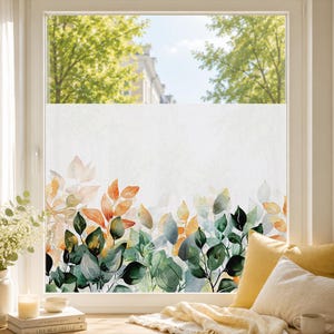 Könnte beinhalten: Eine Fensterfolie mit halbtransparenter, mattierter Oberfläche und einem botanischen Aquarell-Druck im unteren Bereich. Das Design zeigt geschichtete Blätter in Waldgrün, Salbei, gedämpftem Orange und Gelb auf einem weißen Hintergrund.