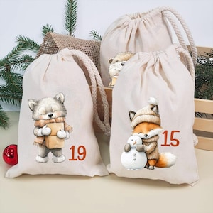 Könnte beinhalten: Zwei cremefarbene Baumwollbeutel mit Kordelzug und festlichen Illustrationen. Ein Beutel zeigt einen grauen Wolf mit einer Schachtel und der orangefarbenen Zahl 19. Der andere Beutel zeigt einen Fuchs mit Mütze, Schal und Schneemann sowie der Zahl 15.