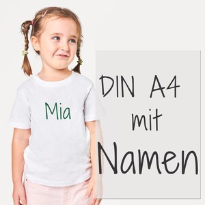 Peut inclure: Un t-shirt blanc à manches courtes avec le prénom Mia imprimé en vert foncé sur la poitrine. À côté du t-shirt se trouve un panneau rectangulaire avec le texte noir DIN A4 mit Namen écrit dans une police de style manuscrit décontracté.