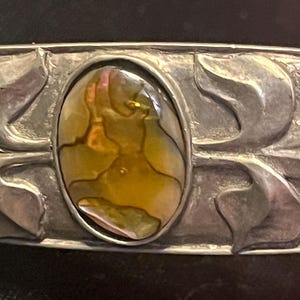 Puede incluir: Una pulsera de plata con una incrustación de nácar de abulón iridiscente. La pulsera presenta un diseño floral.