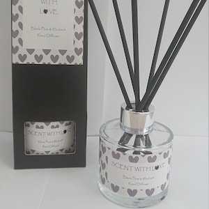 May include: A black and white reed diffuser bottle with a label that reads "Scent with Love Black Plum & Rhubarb Reed Diffuser". The bottle is surrounded by black diffuser sticks.