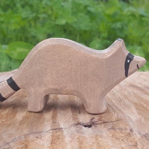 May include: A wooden raccoon figurine with black and white stripes on its tail. The figurine is painted a light brown color and has black eyes.