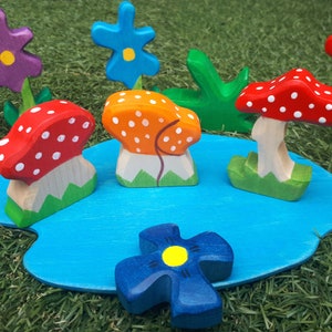 May include: A wooden toy set featuring a blue pond, three red and white mushrooms, two blue flowers, a red flower, an orange flower, and a bee. The set is designed for imaginative play and early childhood development.